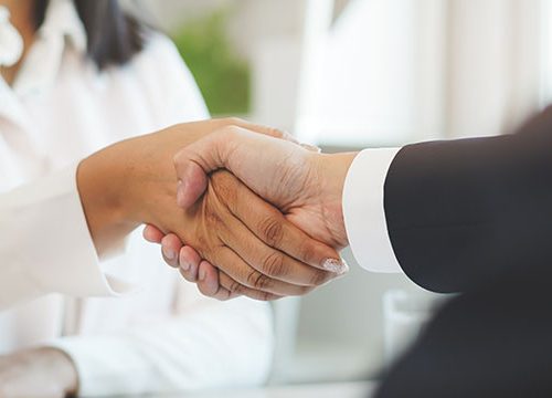Close up of a man in a suit and a woman in a white shirt shaking hands.