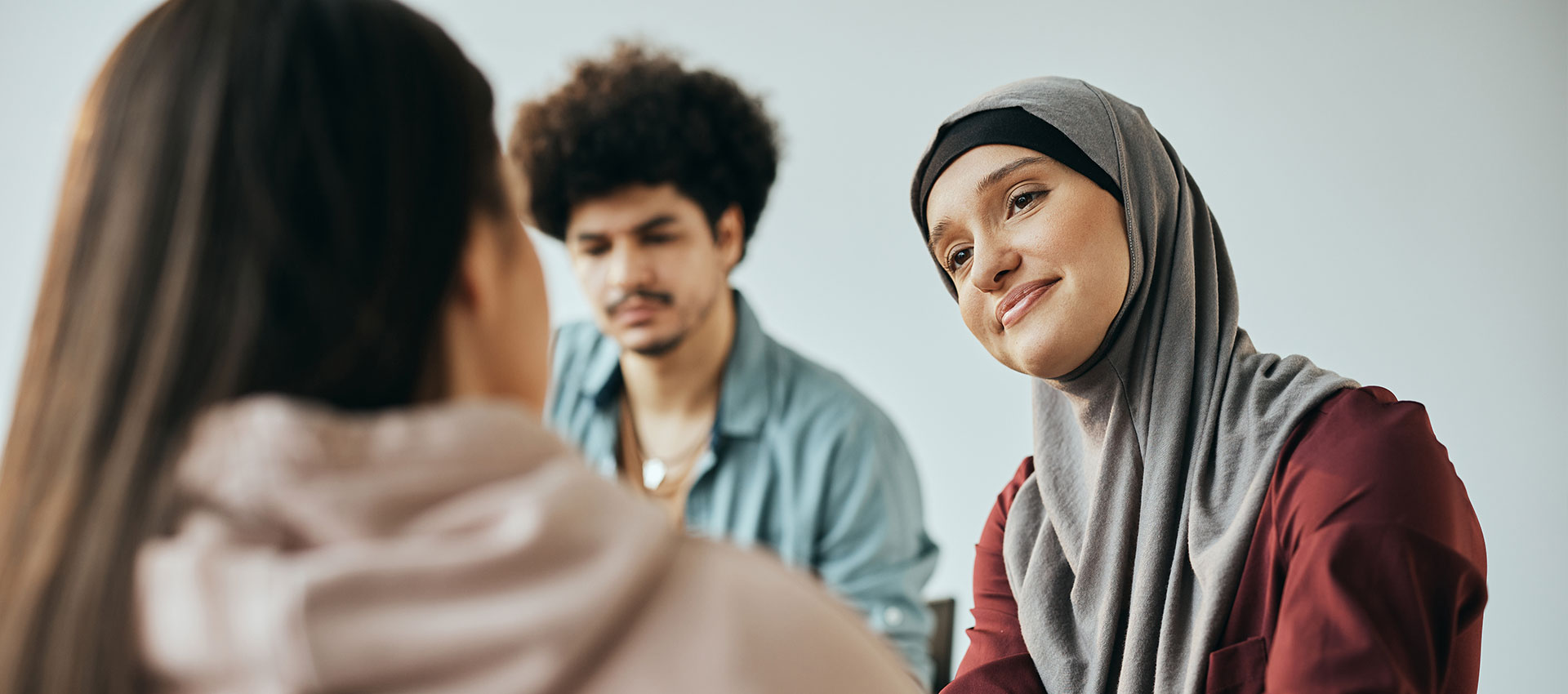 A woman wearing a hijab sits next to a man while talking to a girl in a pink hoody.