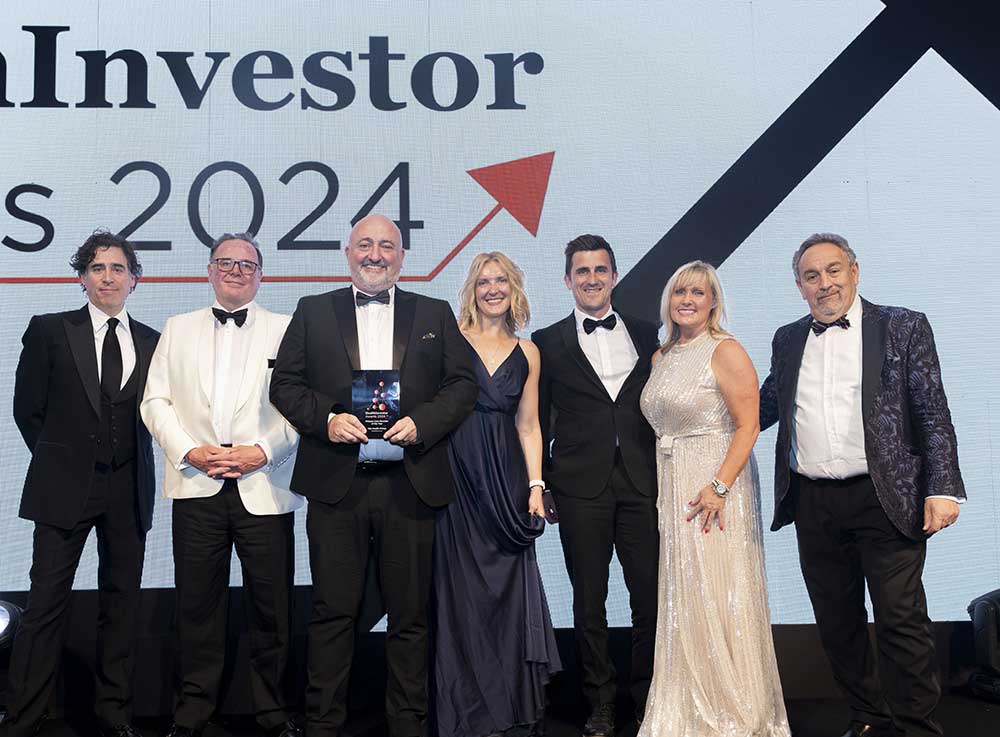 Seven people in formal attire stand onstage, smiling, with one holding an award. Behind them, large text reads "Fund Investor Awards 2024" with an upward red arrow graphic.