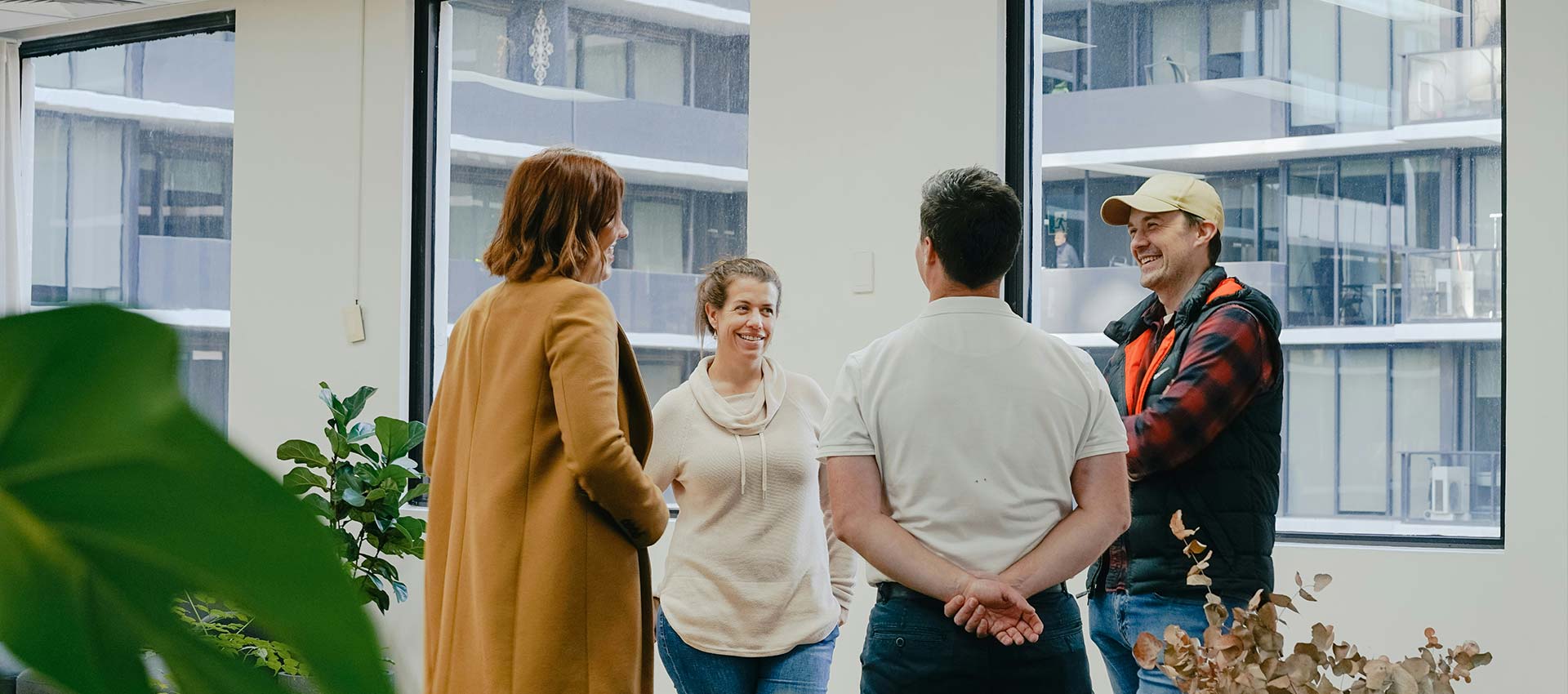 Four people stand in the corridor of a high rise office building talking, laughing and smiling.