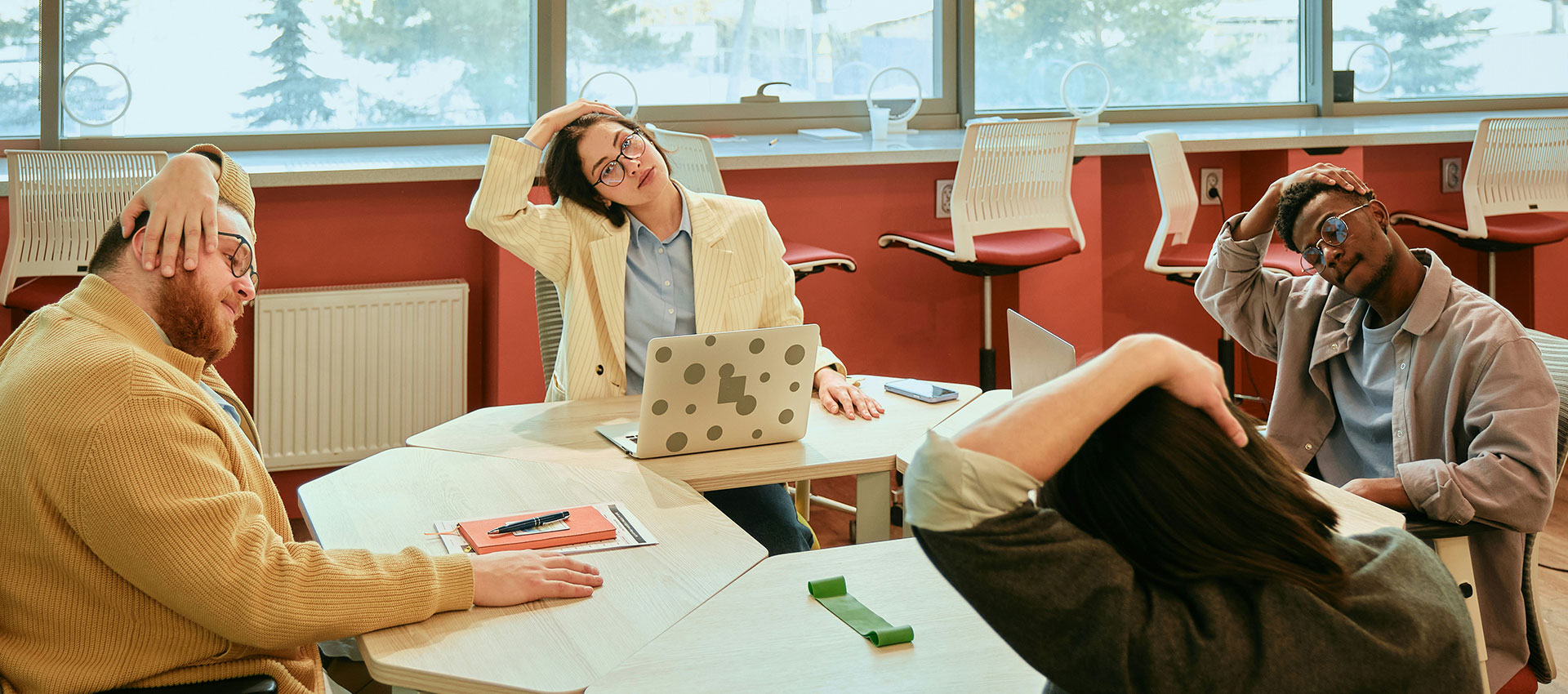 Four people sit around a desk doing neck stretches.