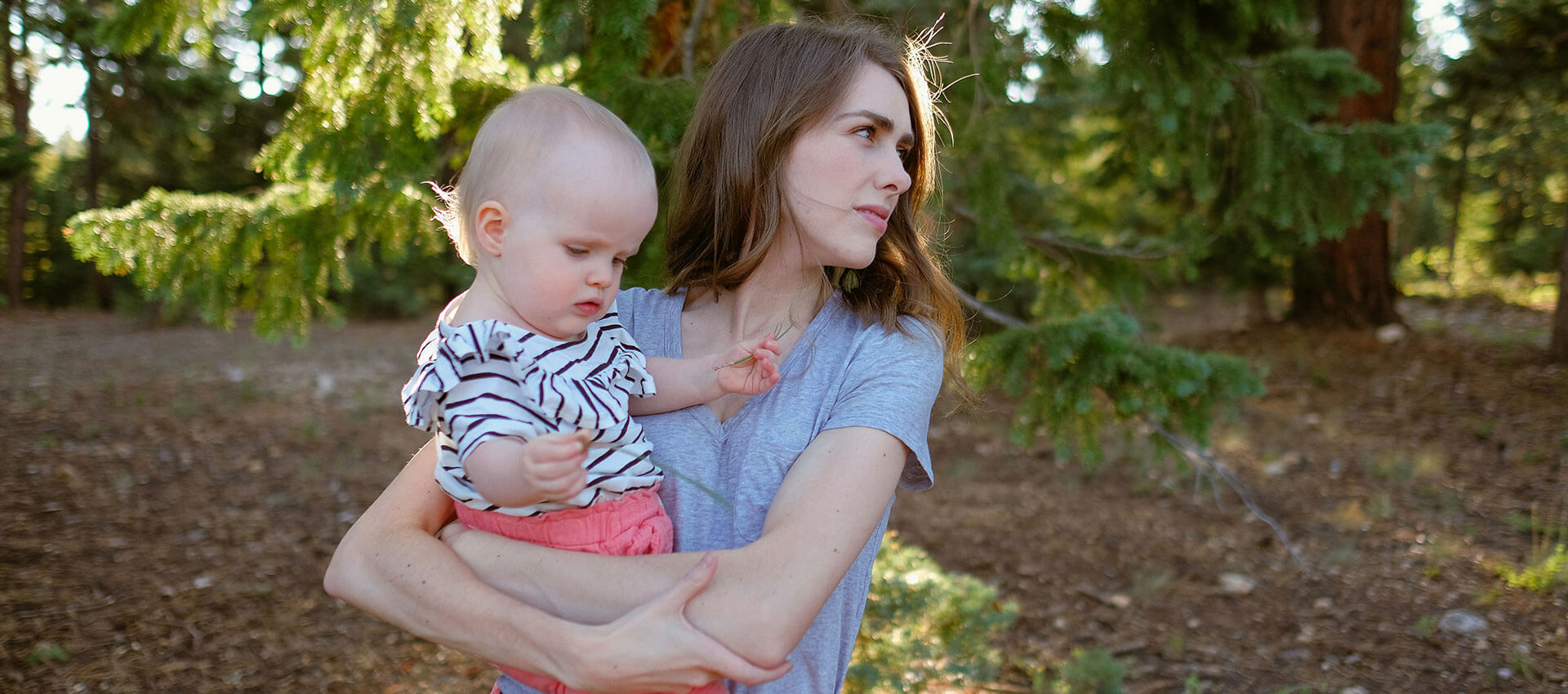 A woman carries a baby girl through a park.