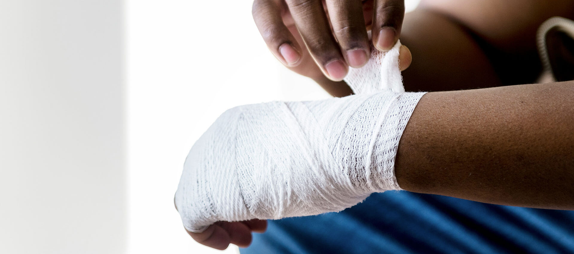 Hands wrap a white bandage around a person's wrist in a well-lit room, suggesting a focus on care and healing. One hand secures the bandage tightly.