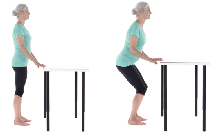 A person in light exercise attire stands upright behind a table in the first image, then bends knees slightly in the second. The table is situated in a plain, white space.
