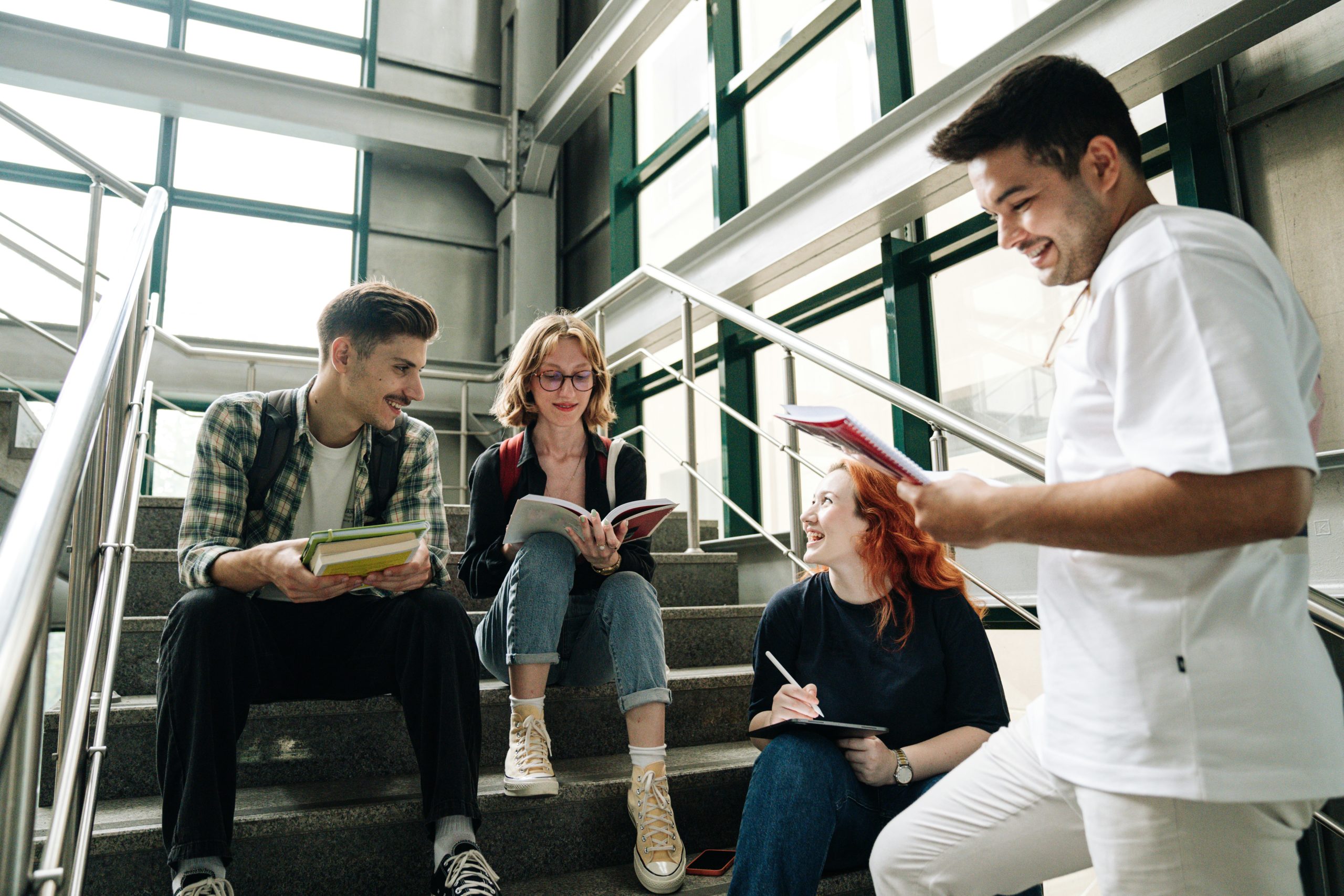 A group of student sit on a stairwell inside a university, talking and comparing notes.