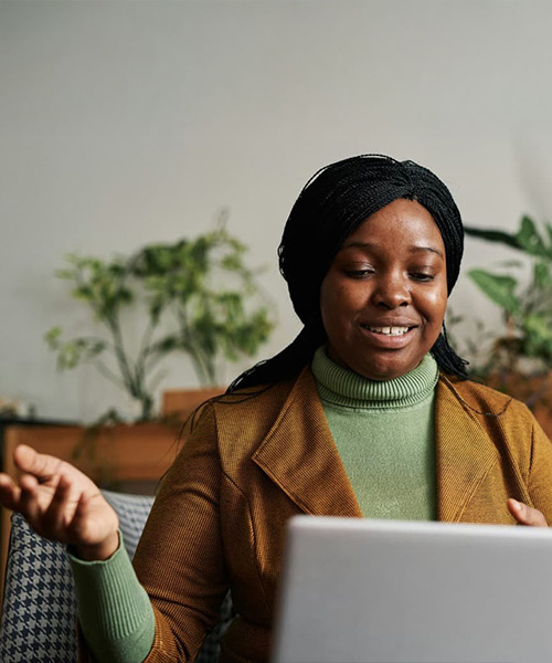A woman talking to a laptop whilst sitting on a chair in a cozy room.