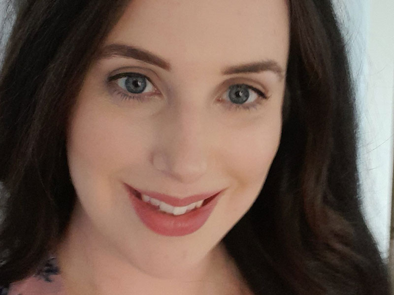 A close up image of a woman with dark brown hair smiles at the camera.