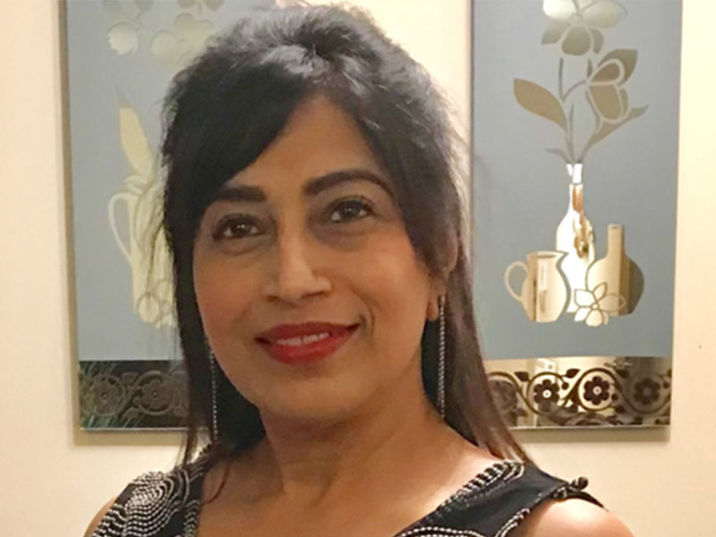 A woman with dark brown hair wearing red lipstick smiles into the camera.