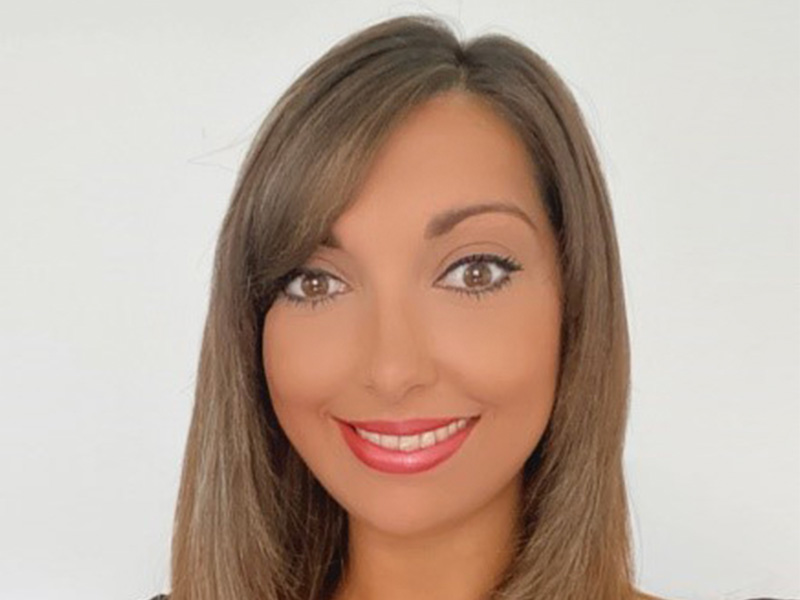 A young woman with light brown hair looks into the camera and smiles.