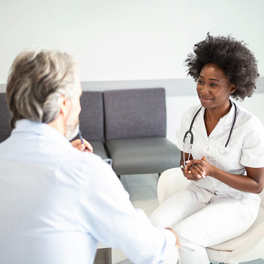 A healthcare professional with a stethoscope engages with a seated person in an office, suggesting a consultation setting.