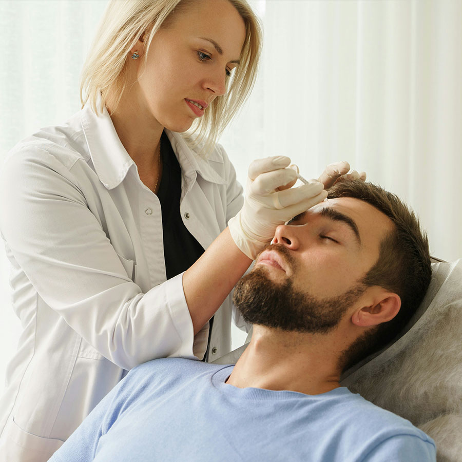 Healthcare professional administers an injection to a patient's forehead in a clinical setting with white curtains in the background.