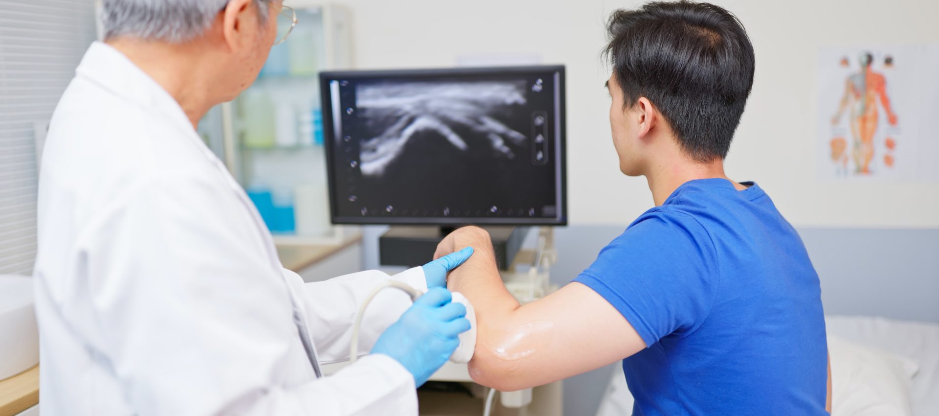 side back view asian young man undergoing ultrasound for elbow pain from sports accident sit in medical examination room