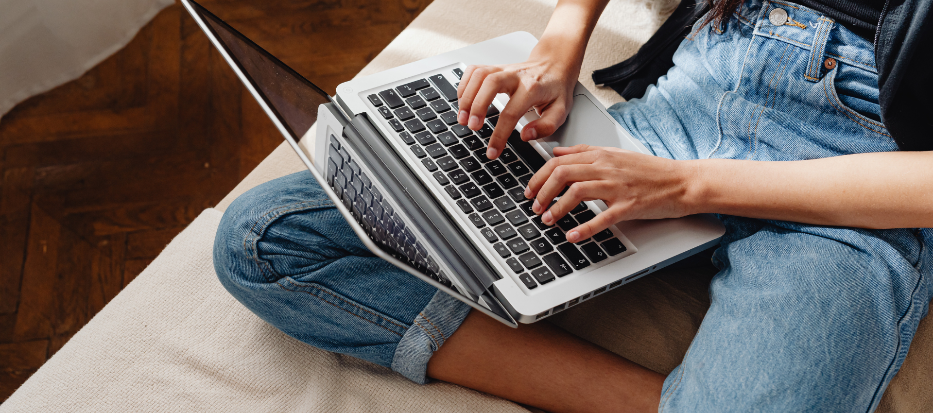 A person sitting with crossed legs on a sofa, typing on a laptop resting on their lap.
