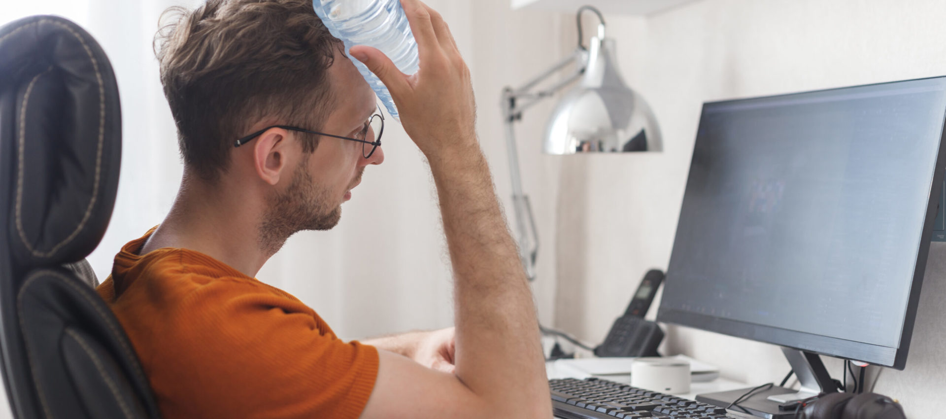 Working at home man suffering from heat and thirst cools down with water bottle at hot summer day